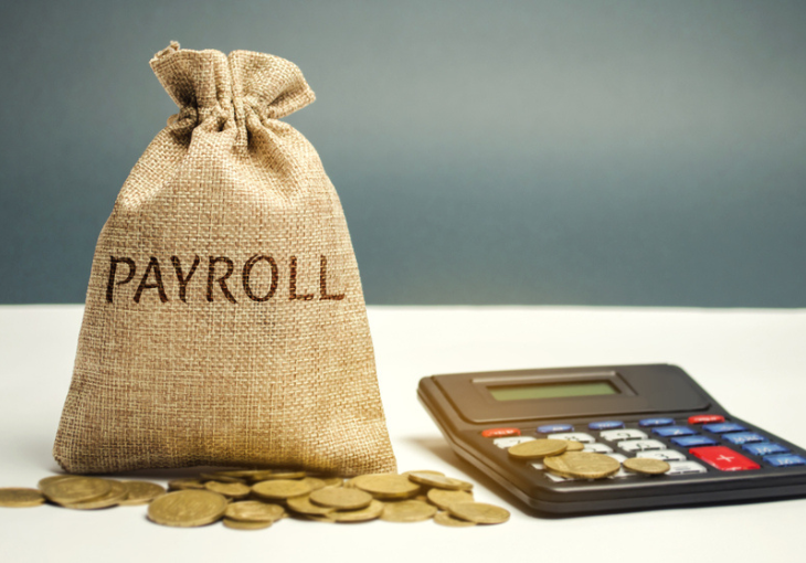 small sack with payroll on it. pile of coins in front an a calculator on the right of the sack